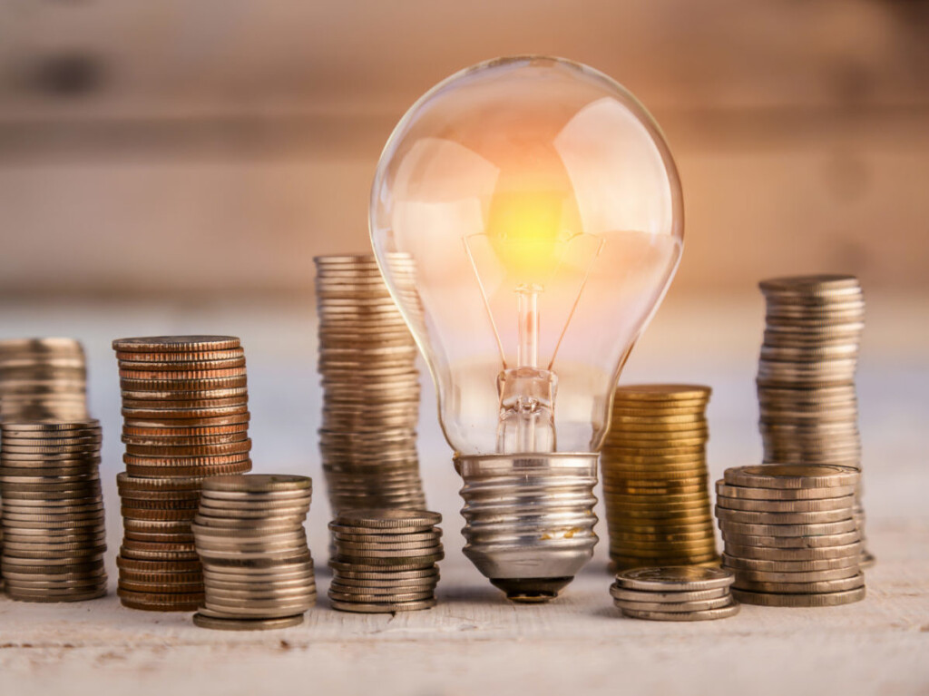 Glowing Light Bulb Among Many Coins